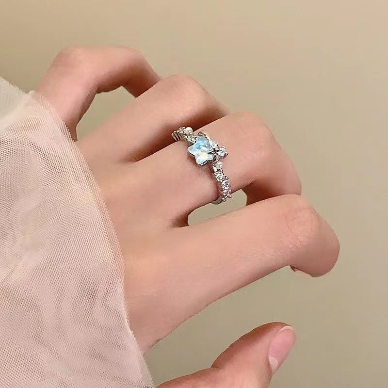 Hand wearing a silver ring with a blue gemstone on a beige background