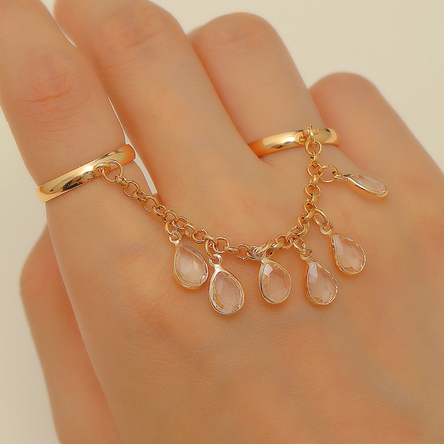Gold ring with teardrop-shaped gemstones on a hand against a neutral background