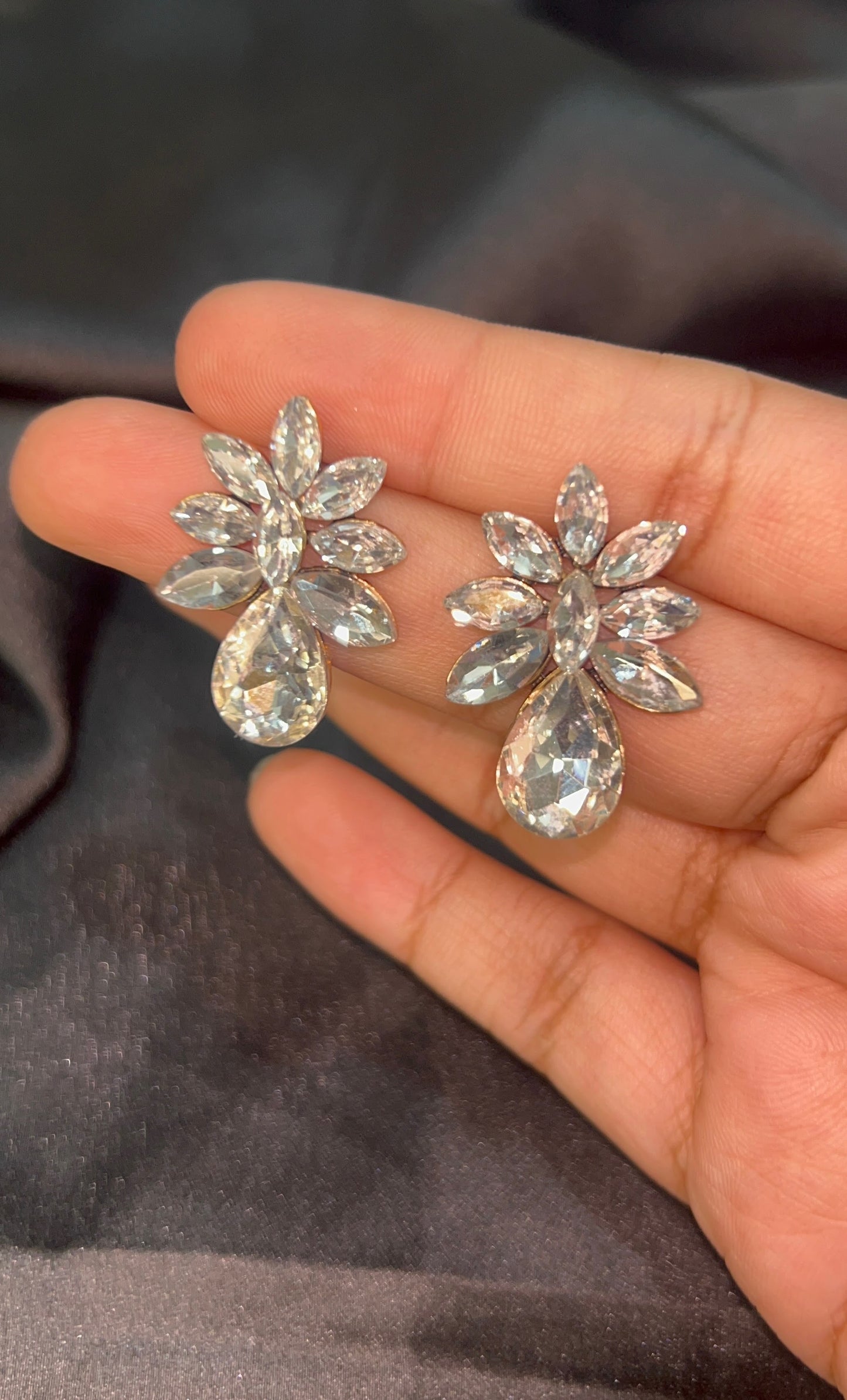 Pair of silver floral earrings held in a hand against a dark fabric background
