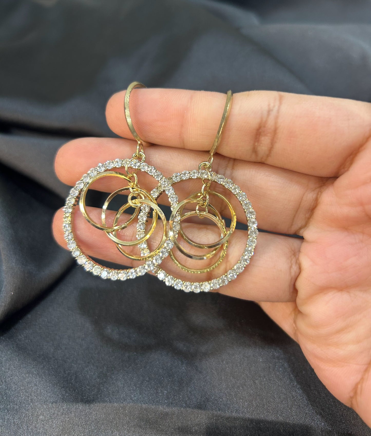 Gold and silver hoop earrings held between fingers against a dark background