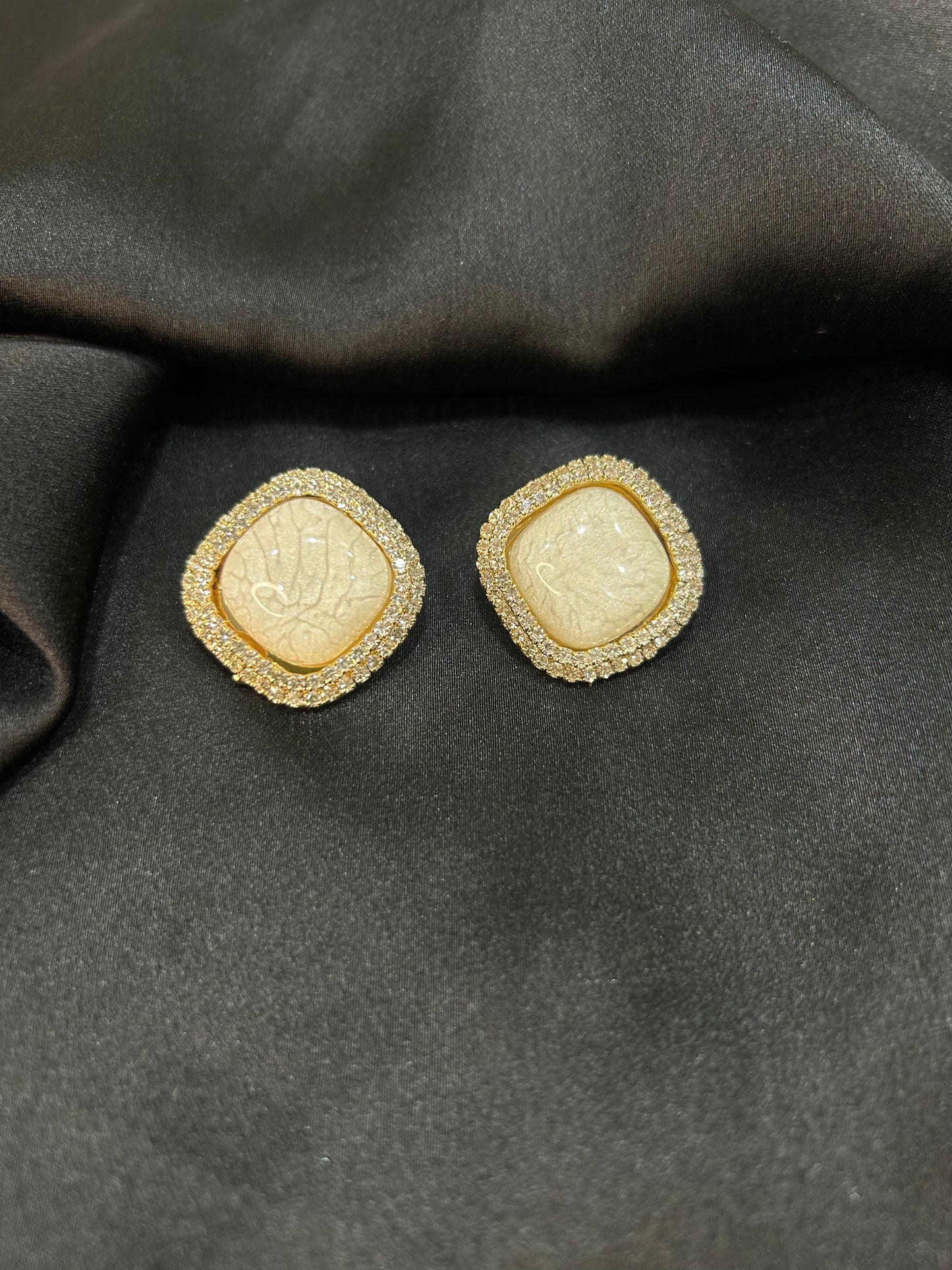 Pair of gold earrings with central stone on a dark fabric background