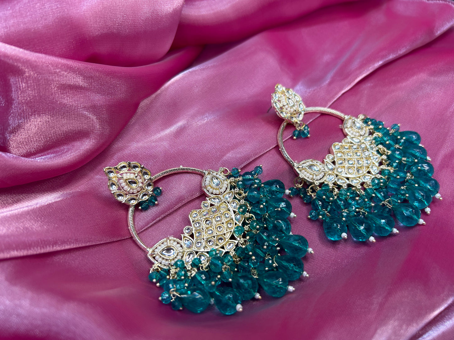 Pair of teal and gold earrings on a pink fabric background