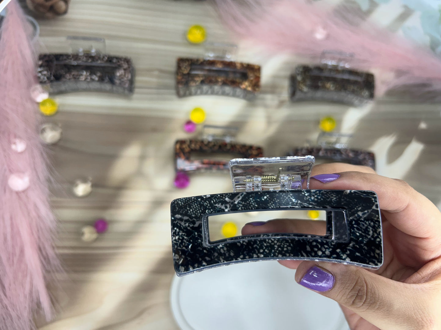 Hand holding a black and silver hair clip with a blurred background of similar clips.