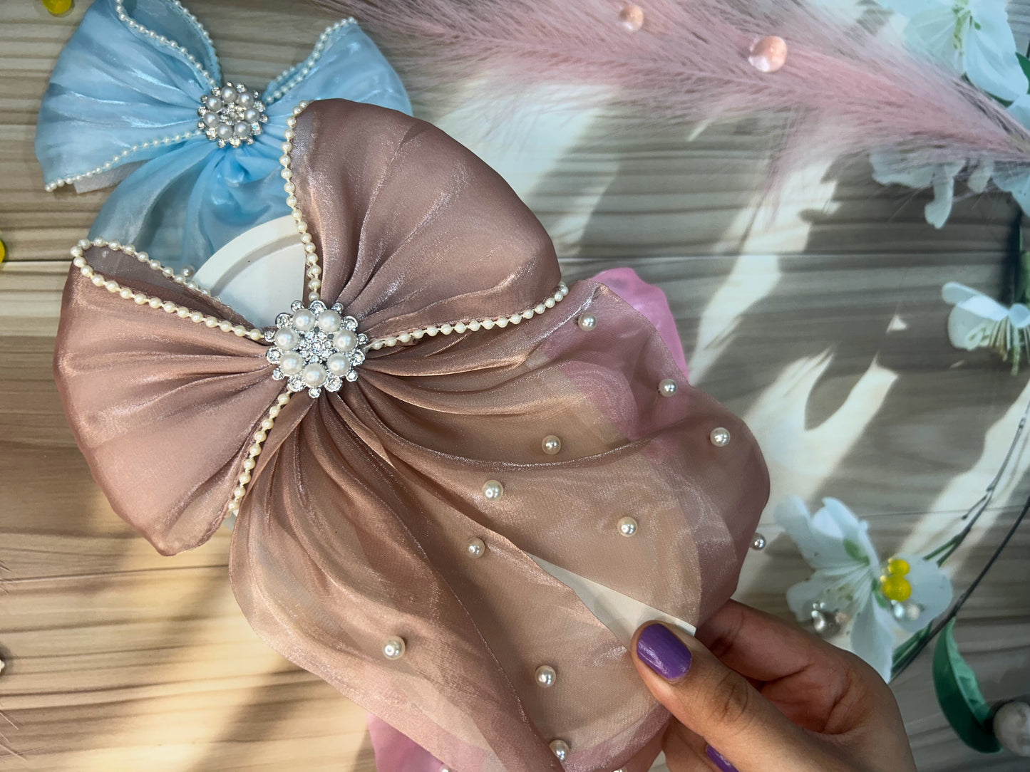 Decorative headband with a large bow and pearl embellishments held by a hand.