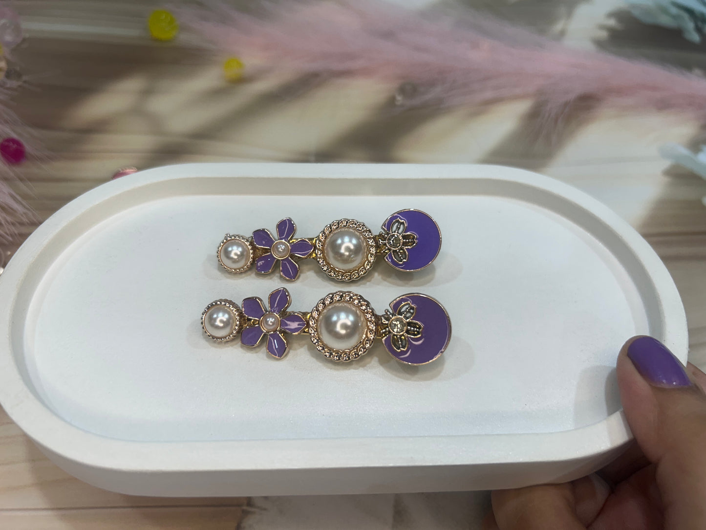 Purple floral hair clip on a white jewelry box with feathers in the background