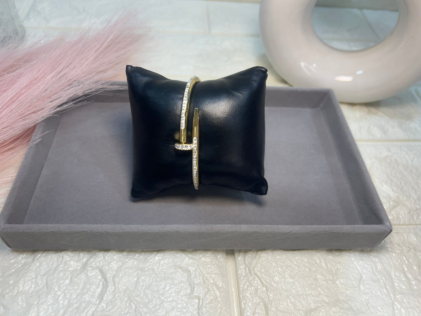 Black leather pillow with a gold bracelet on a gray tray