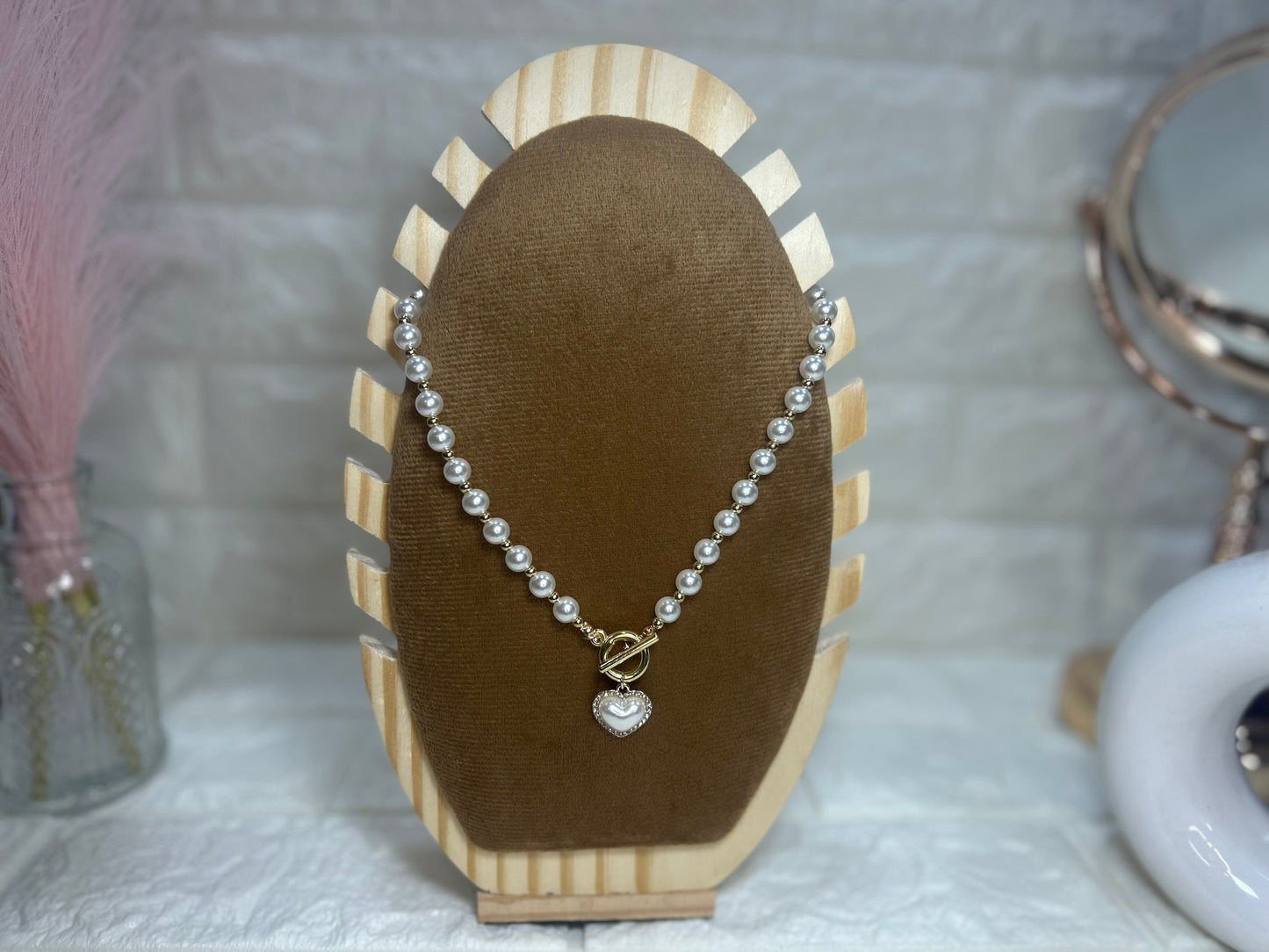 Pearl necklace with a heart charm on a brown jewelry display stand.