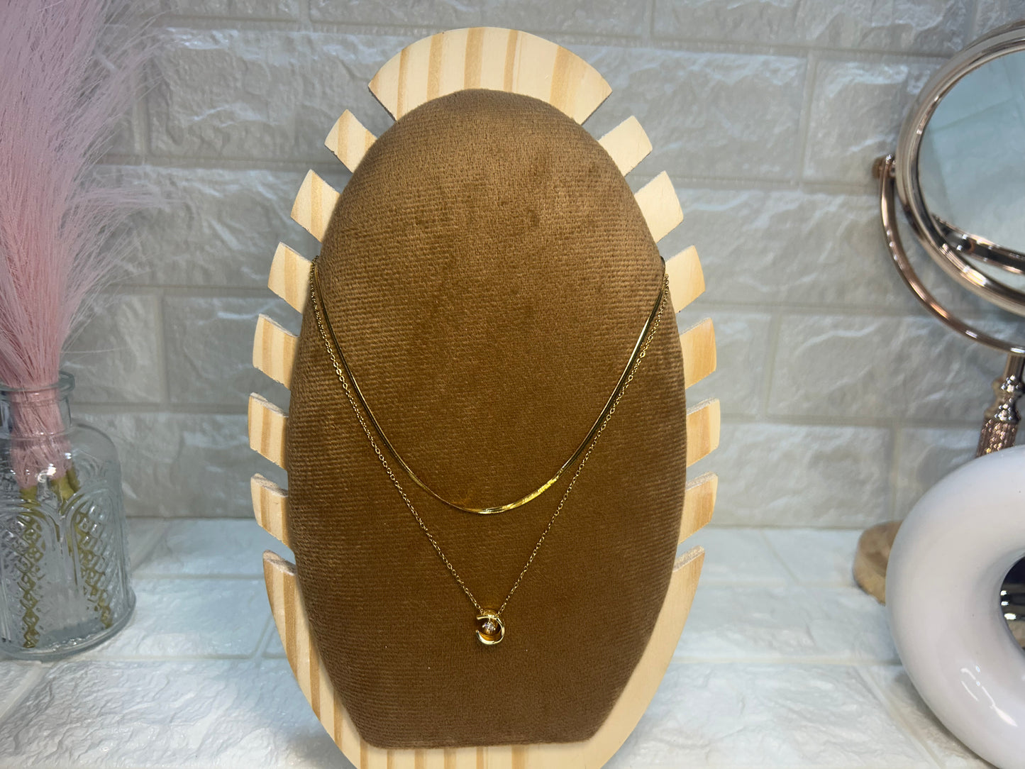 Gold necklace on a brown velvet display stand with a decorative background