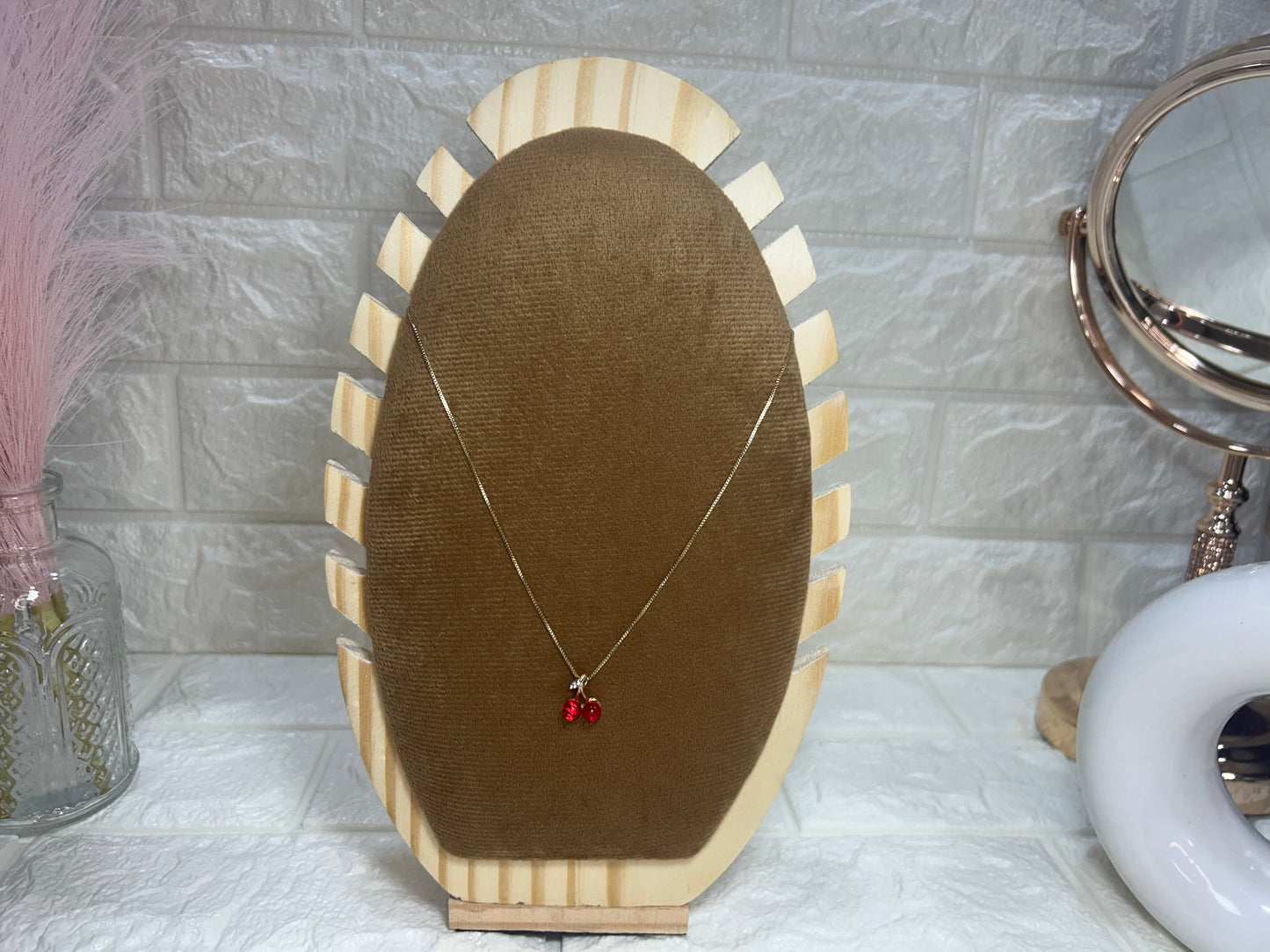 Necklace with red pendants on a wooden stand against a tiled wall.