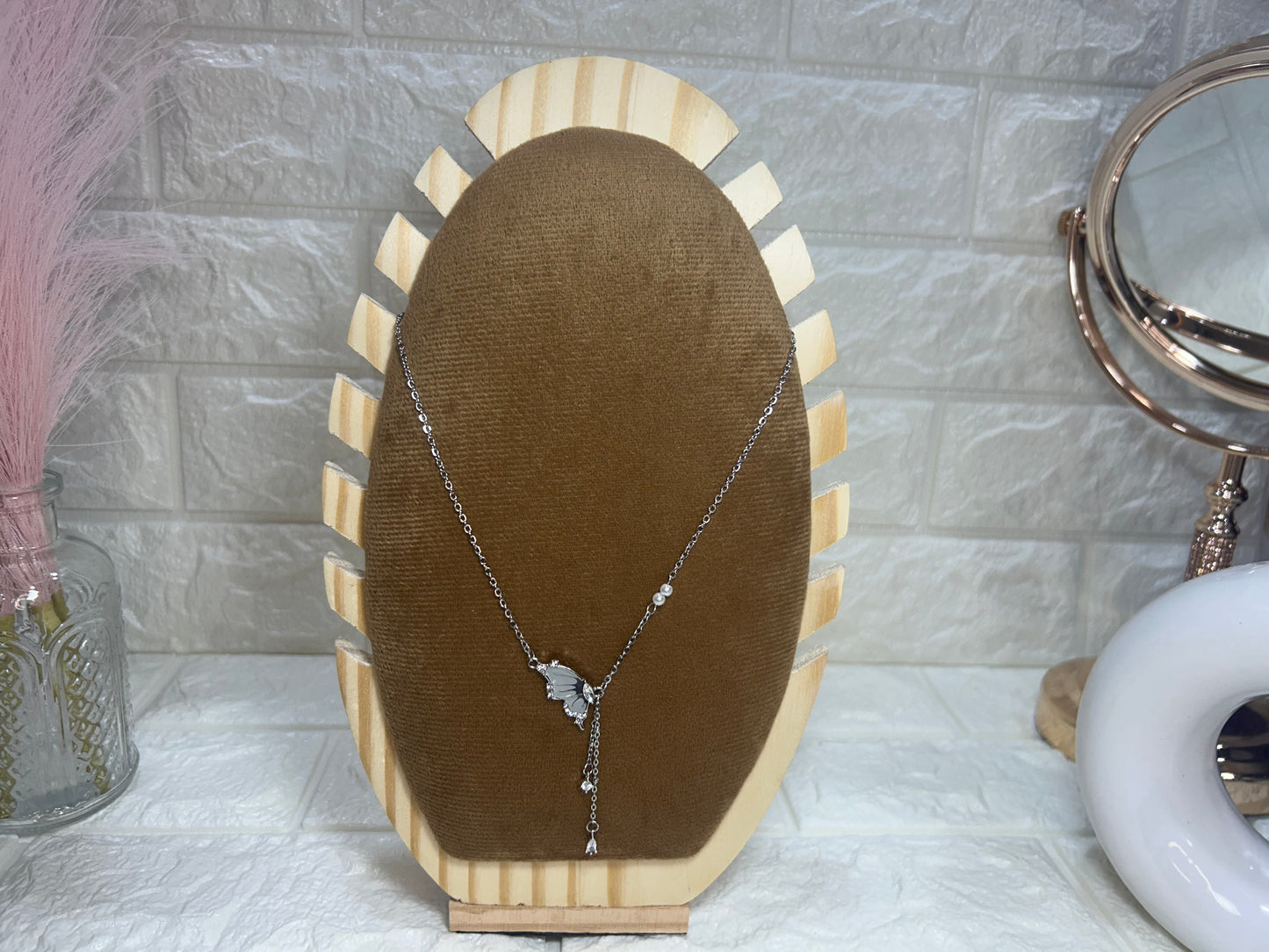 Necklace on a brown velvet cushion with a wooden stand against a textured wall.