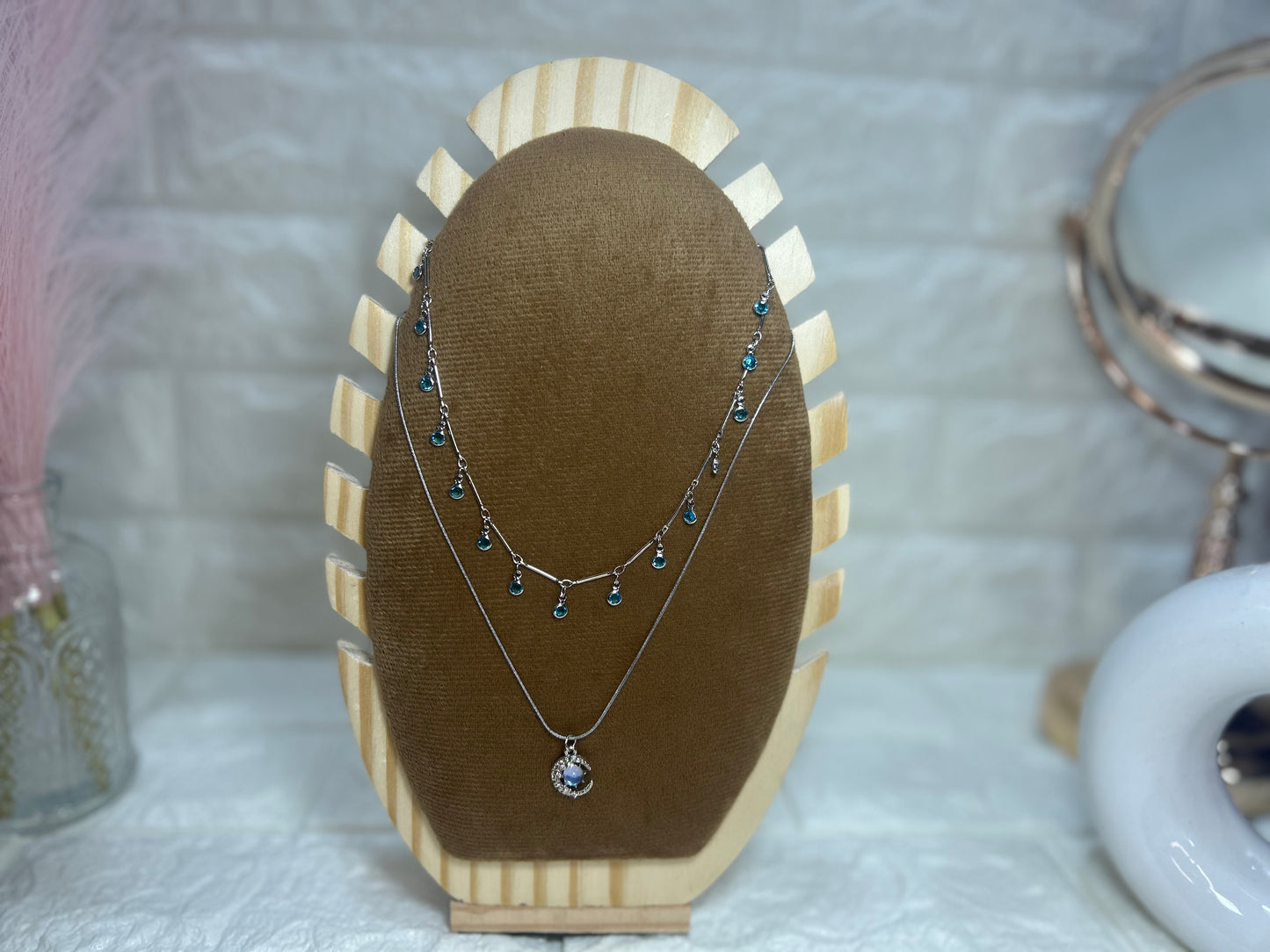Two necklaces on a brown velvet stand with a white textured background