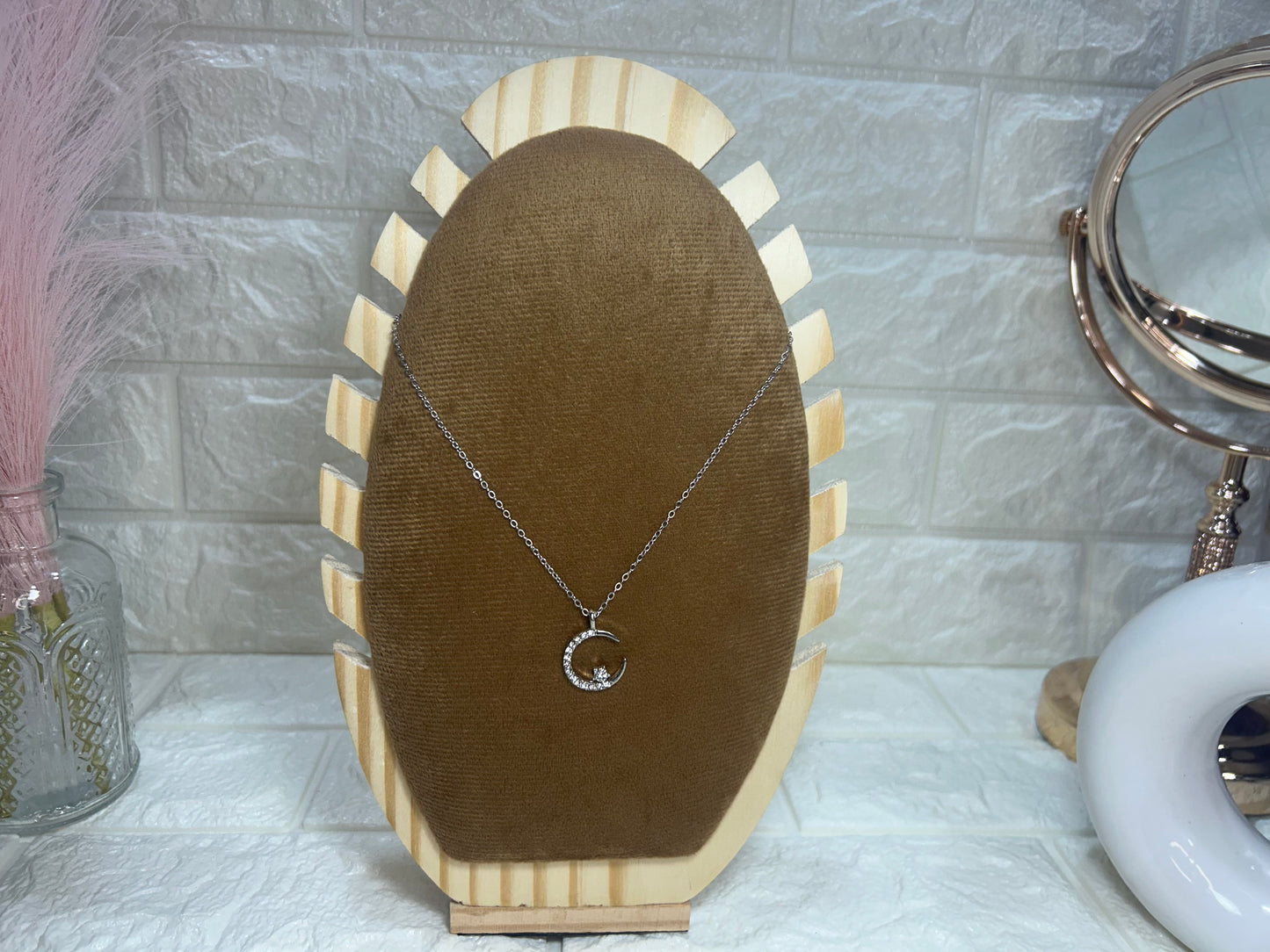 Necklace with a moon design on a wooden and brown fabric stand against a light gray tiled wall.