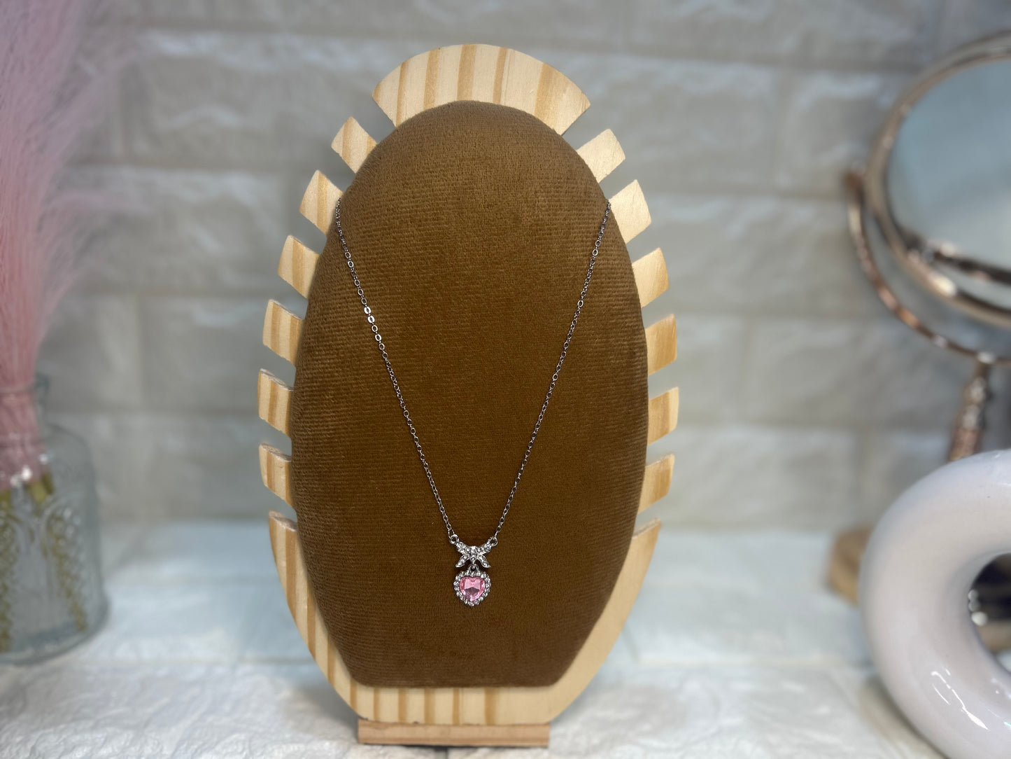 Necklace with a pink pendant on a brown velvet stand against a blurred background