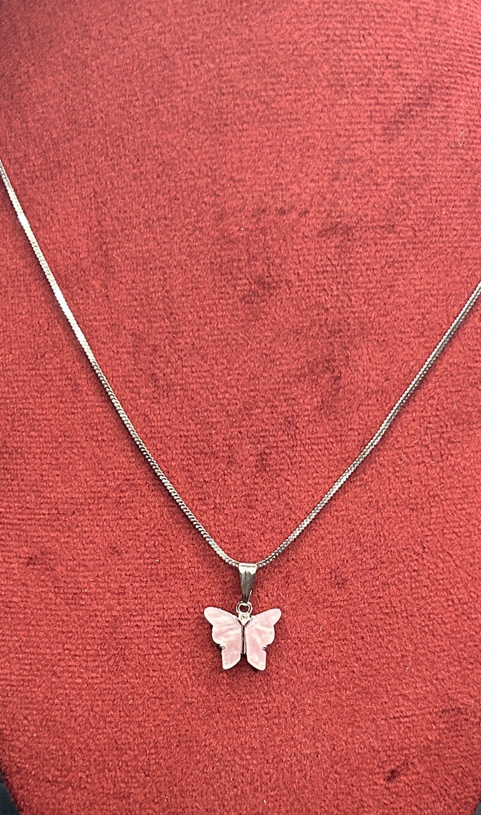 Butterfly pendant necklace on a red mannequin bust with a geometric patterned background