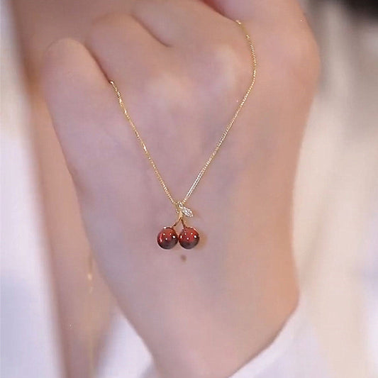 Gold necklace with cherry pendant on a blurred background