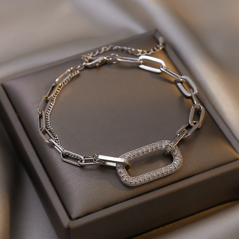 Silver chain bracelet with a diamond-encrusted clasp on a brown surface