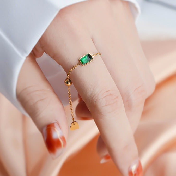 Gold ring with a green gemstone on a person's finger against a soft background