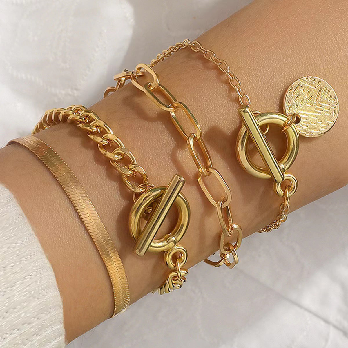 Gold bracelets with various designs on a wrist against a white background
