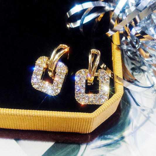 Gold hoop earrings with clear stones on a yellow box with ribbons.