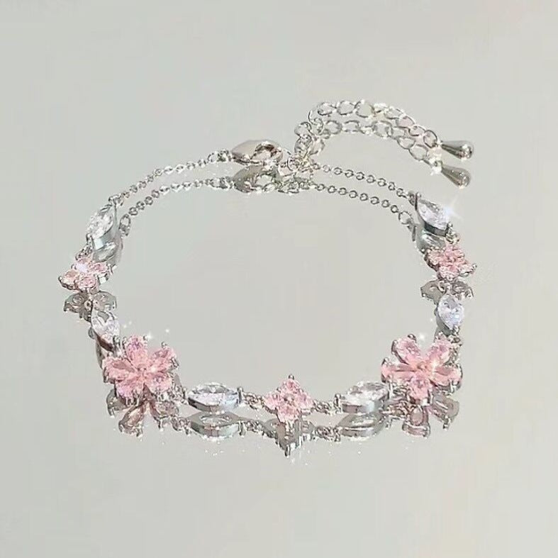Silver bracelet with pink floral charms on a light gray background
