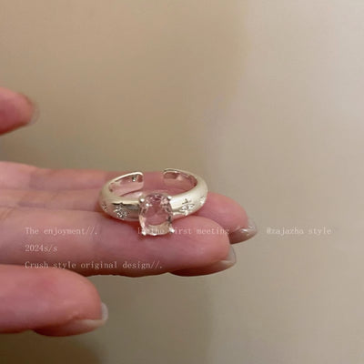 Silver ring with a clear gemstone held in a hand against a neutral background