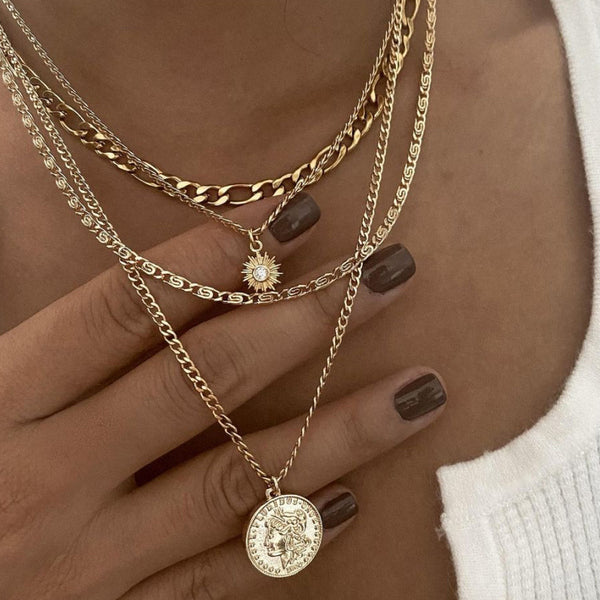 Gold chain necklaces with pendants on a hand with dark nail polish.
