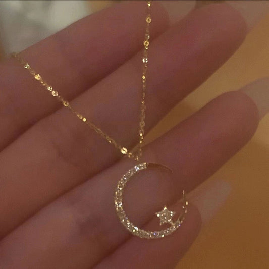 Gold necklace with a crescent moon and star pendant held in hand against a blurred background