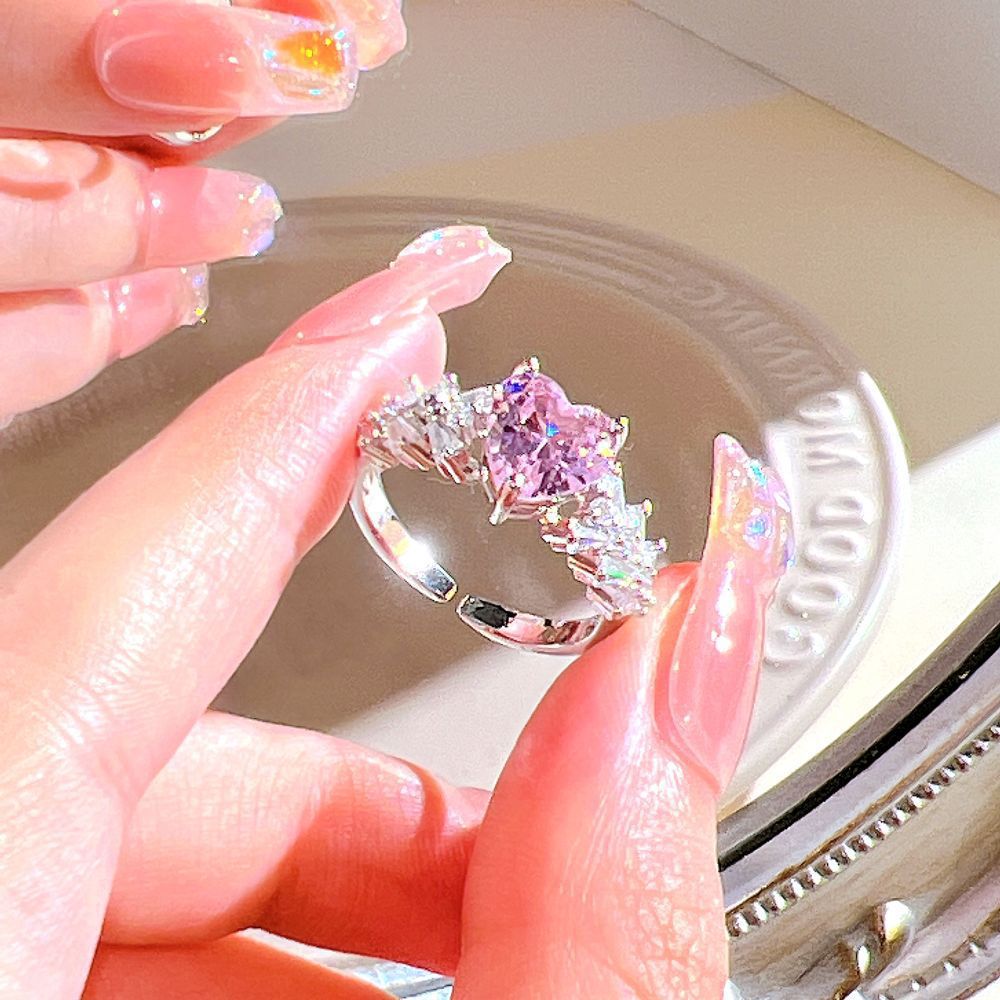 Hand holding a silver ring with a pink gemstone against a blurred background