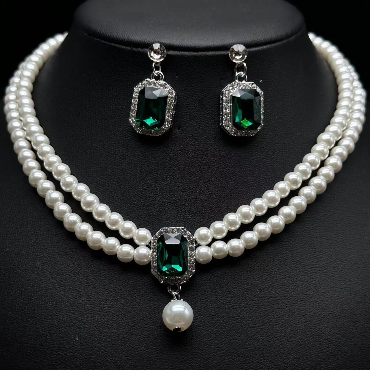 Pearl necklace and earrings with green gemstones on a black background