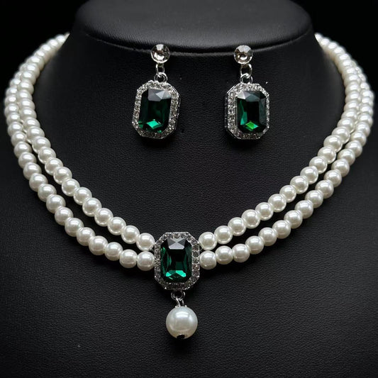 Pearl necklace and earrings with green gemstones on a black background