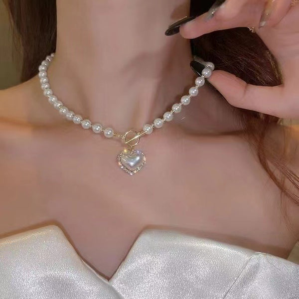Pearl necklace with a heart-shaped charm being adjusted by a hand.