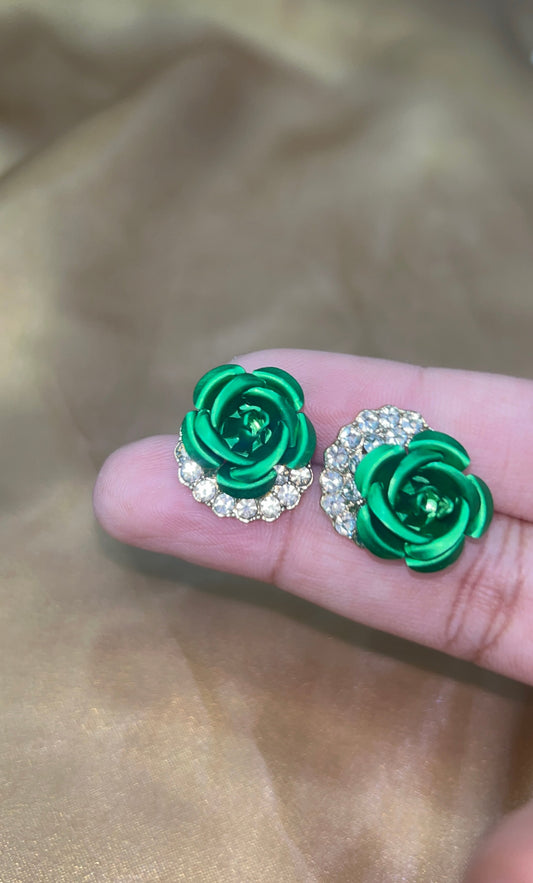 Green rose-shaped earrings held between fingers on a beige background