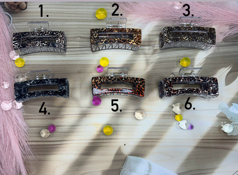 Set of six decorative hair clips on a wooden board with a pink fabric background.