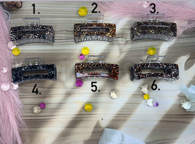 Set of six decorative hair clips on a wooden board with a pink fabric background.