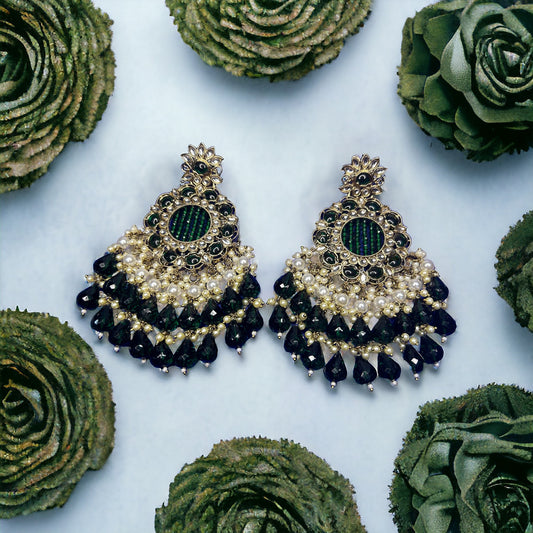 Ornate earrings with black and gold details on a light blue background with green floral decorations.