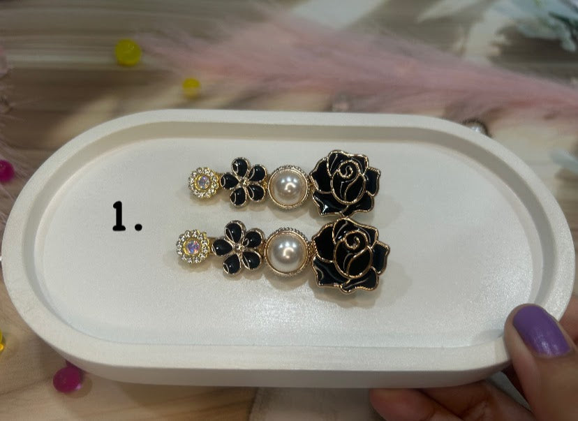 Pair of black and gold floral hair clip on a white tray.