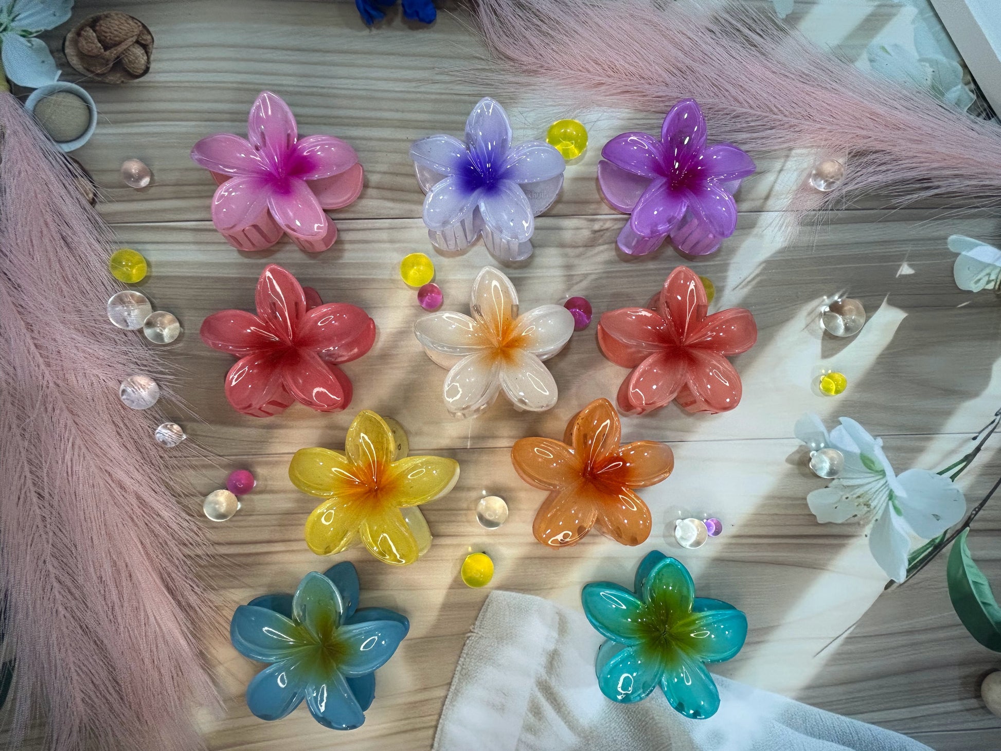 Colorful flower-shaped hair clips on a wooden surface with pink feathers and beads.
