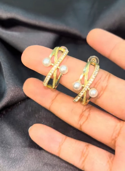 Gold earrings with pearls on a hand against a dark fabric background