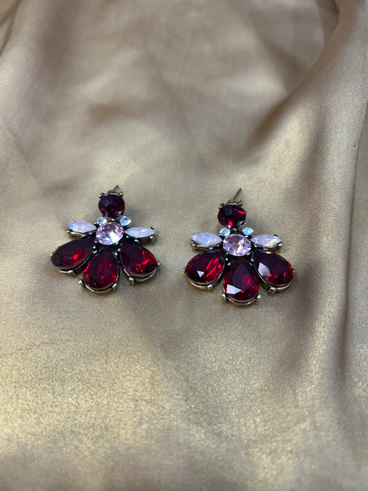 Pair of earrings with red and clear gemstones on a beige fabric background