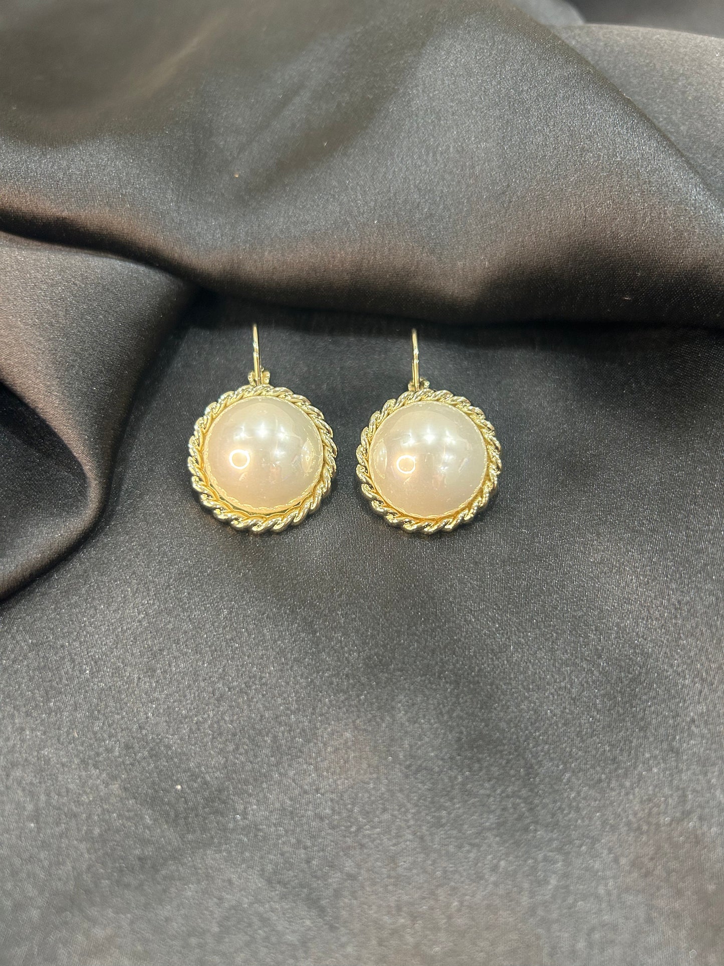 Gold-framed pearl earrings on a gray fabric background