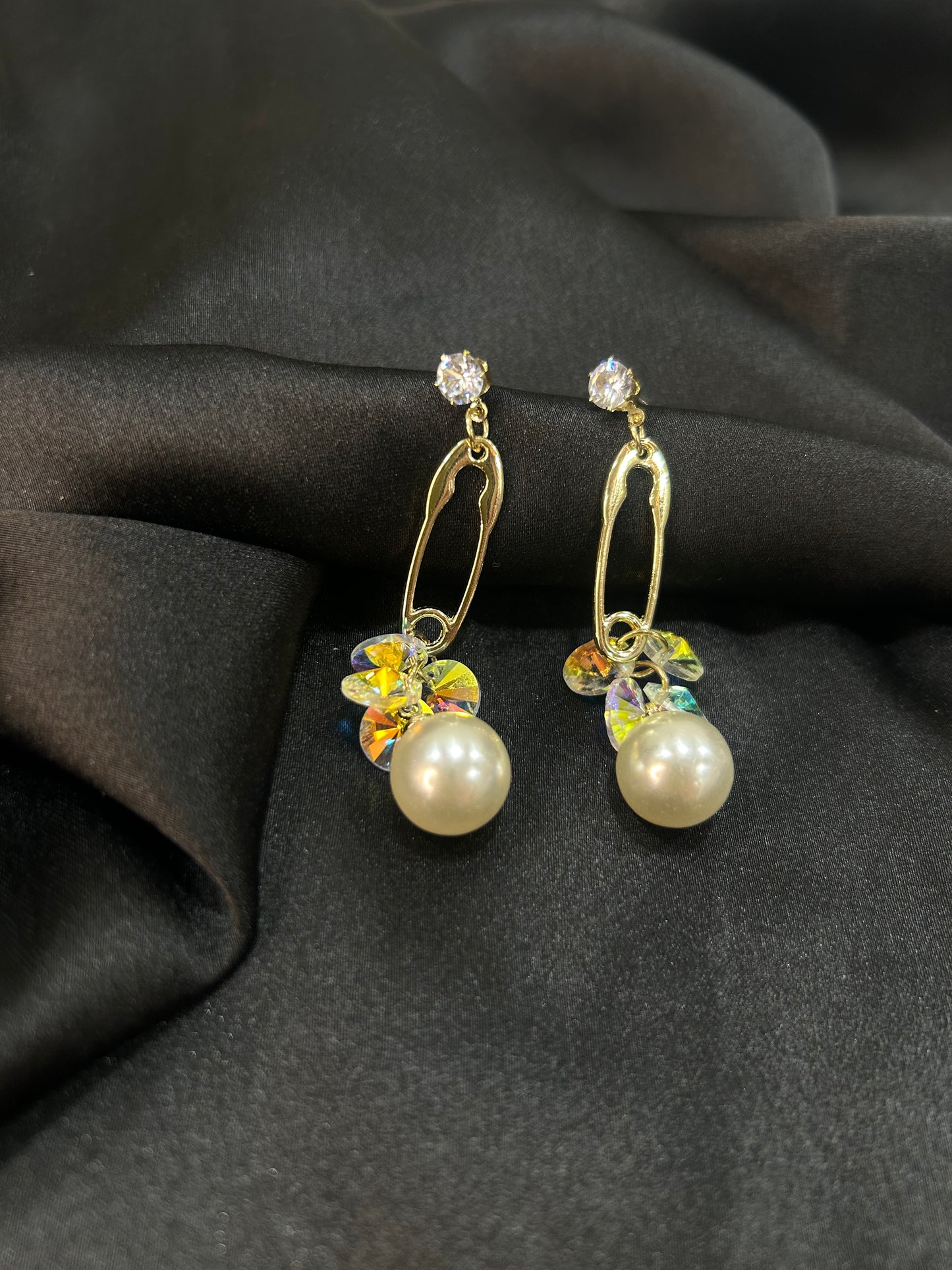 Gold earrings with pearl drops on a black fabric background