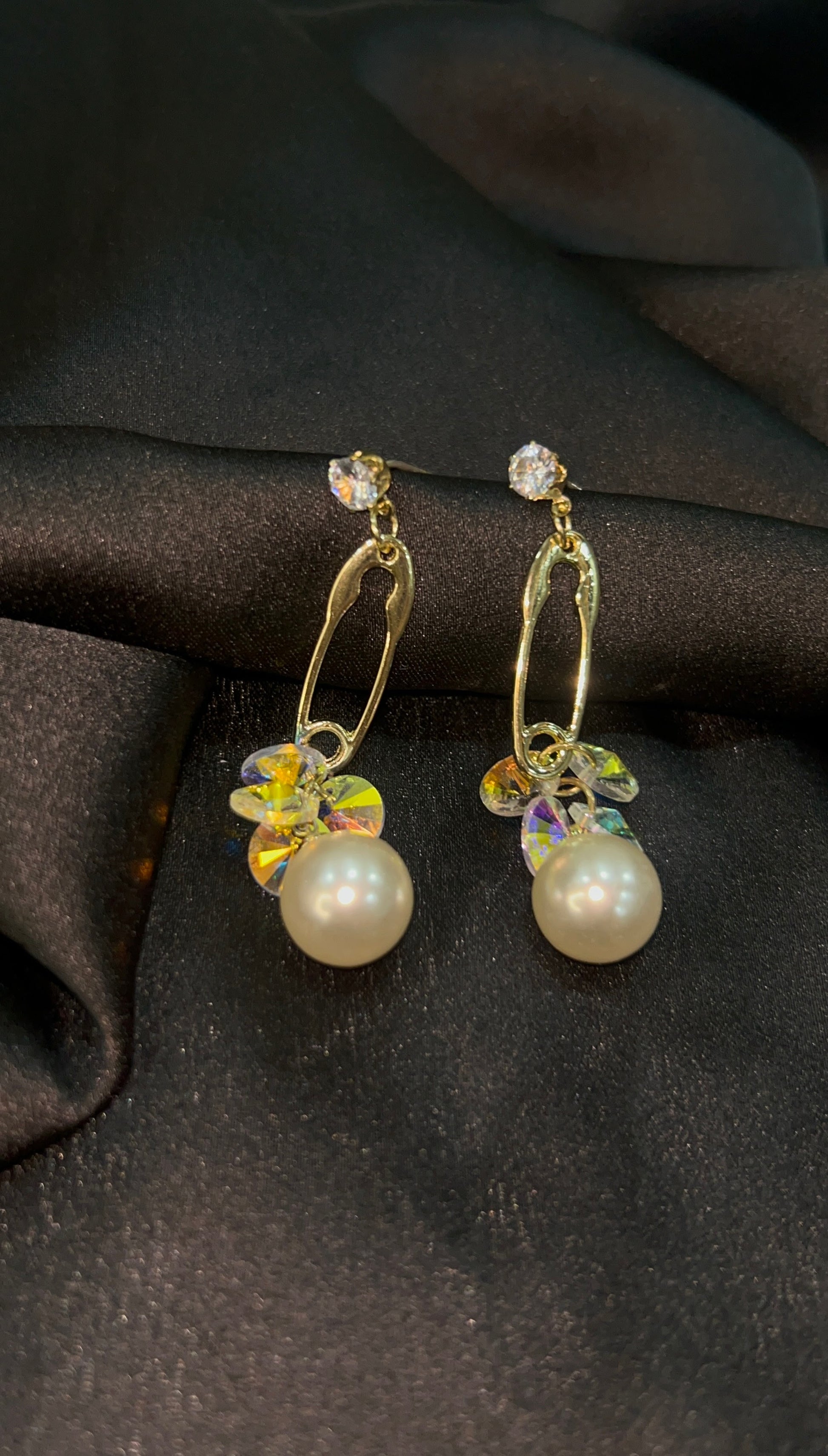 Pair of pearl earrings with gold hooks on a dark fabric background