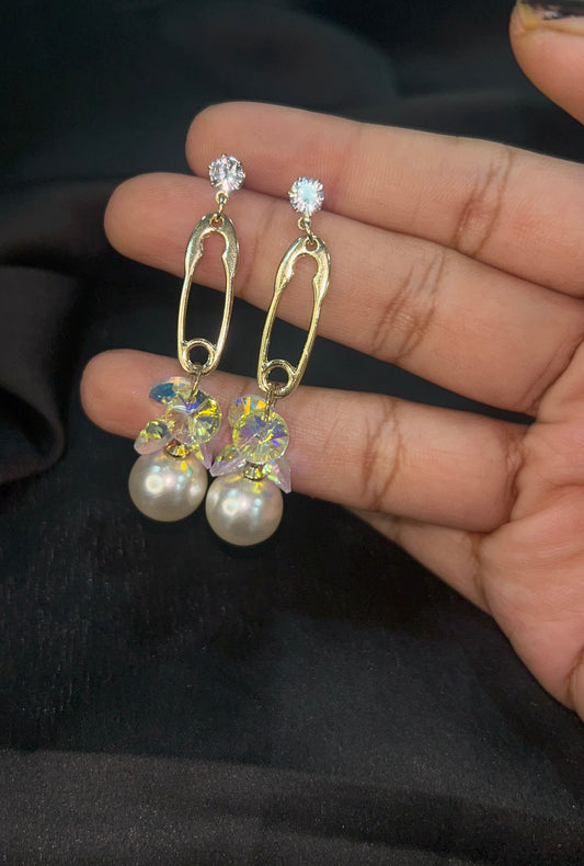 Gold earrings with pearls and crystals held in a hand against a dark background