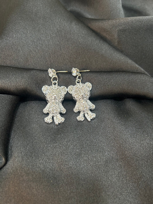 Silver teddy bear-shaped earrings on a gray fabric background