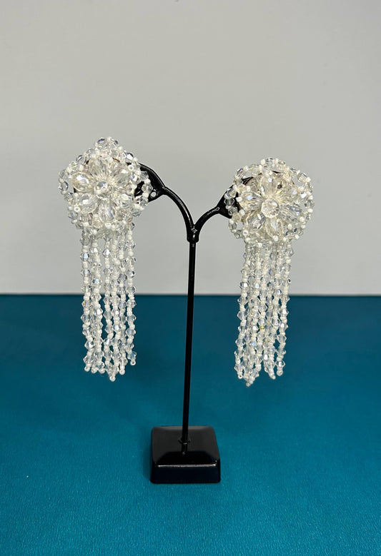 Pair of beaded earrings on a black stand against a gray background