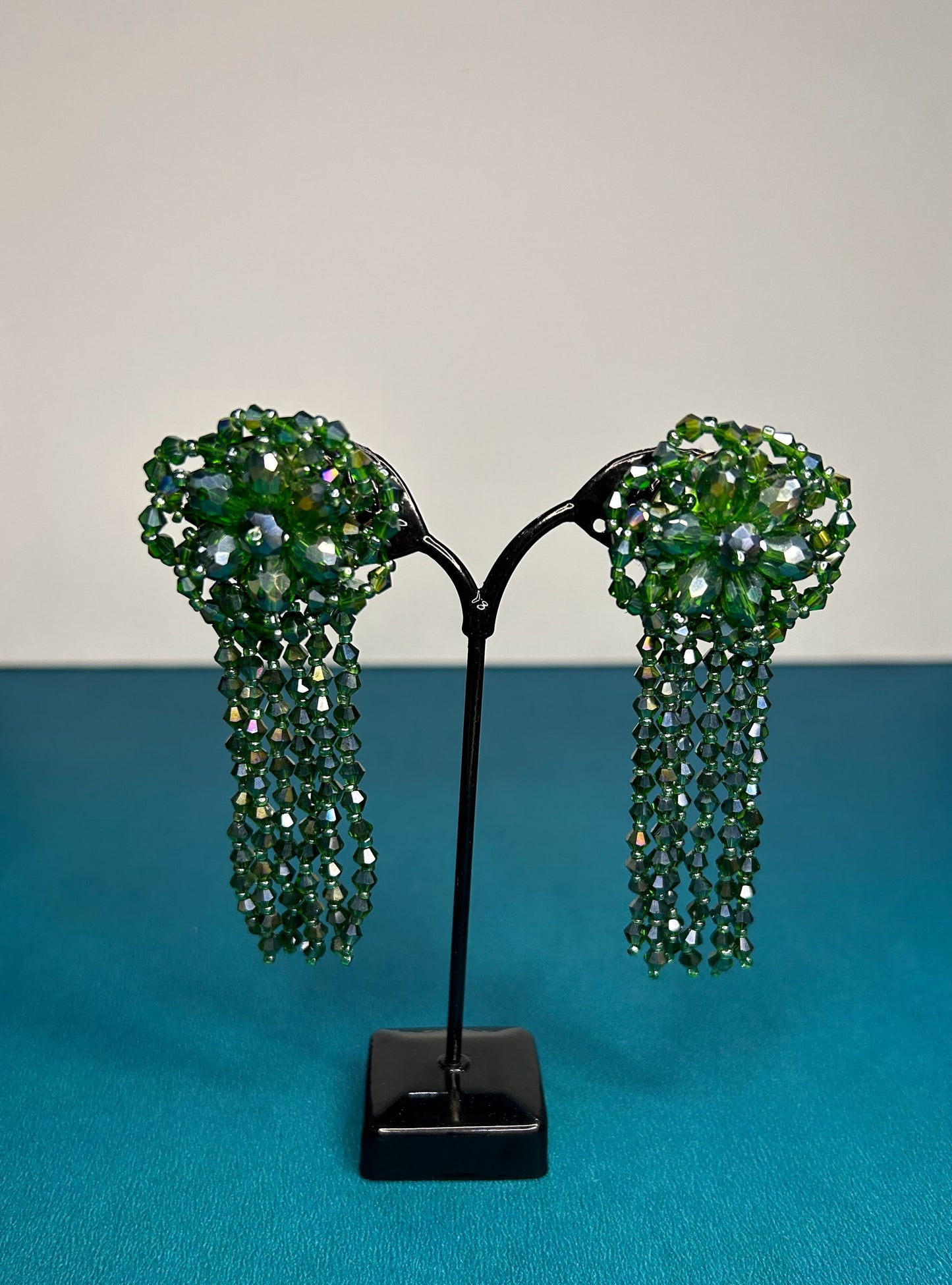 Green beaded earrings on a black stand against a blue and gray background