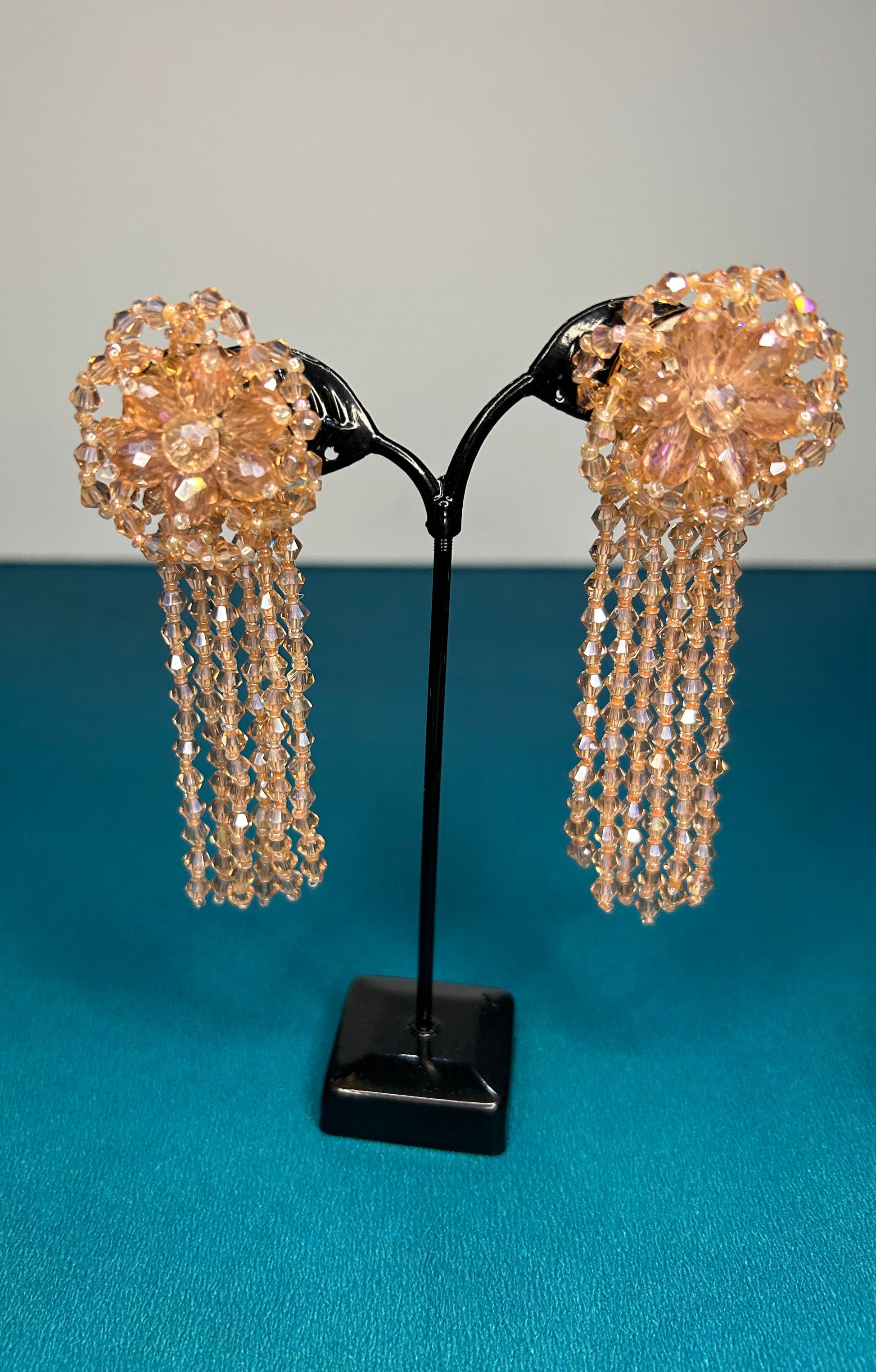 Pair of gold beaded earrings on a black stand against a blue background