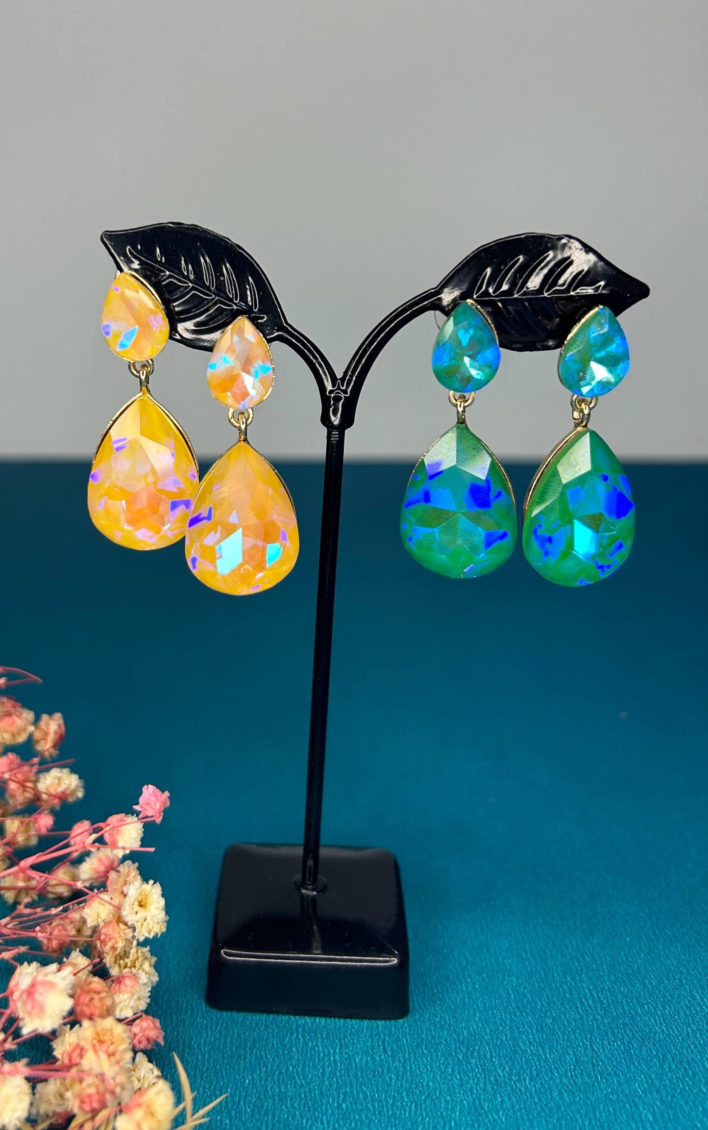 Pair of colorful teardrop earrings on a black stand with a blue background