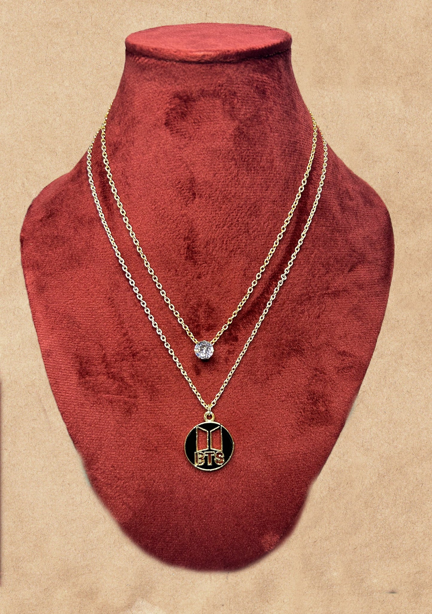 Two gold necklaces on a red velvet bust against a beige background