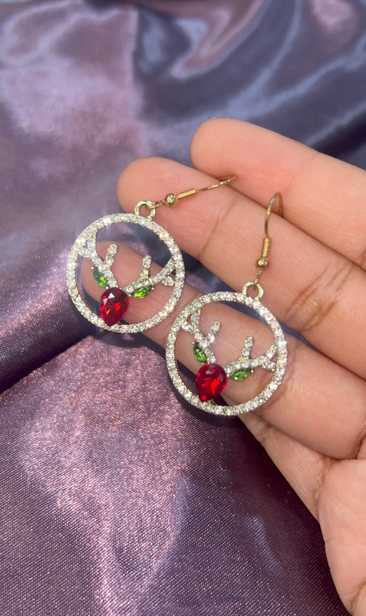 Earrings with red and green accents held against a purple fabric background